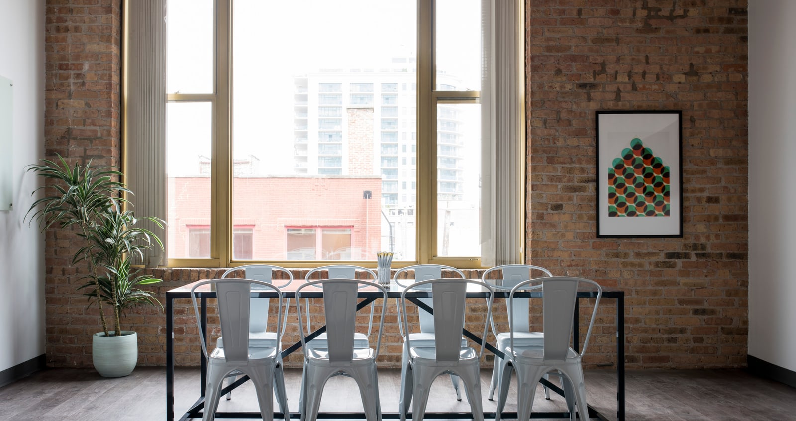 Besprechungstisch mit Metallstühlen vor hohen Fenstern in einem Loft mit Ziegelwand